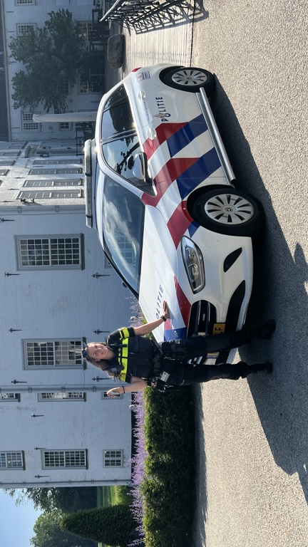 Student Linda staat voor een wit pand bij een politieauto