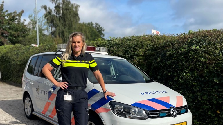 Bettine leunt in uniform tegen een politieauto