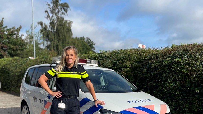 Bettine staat in uniform bij een politieauto