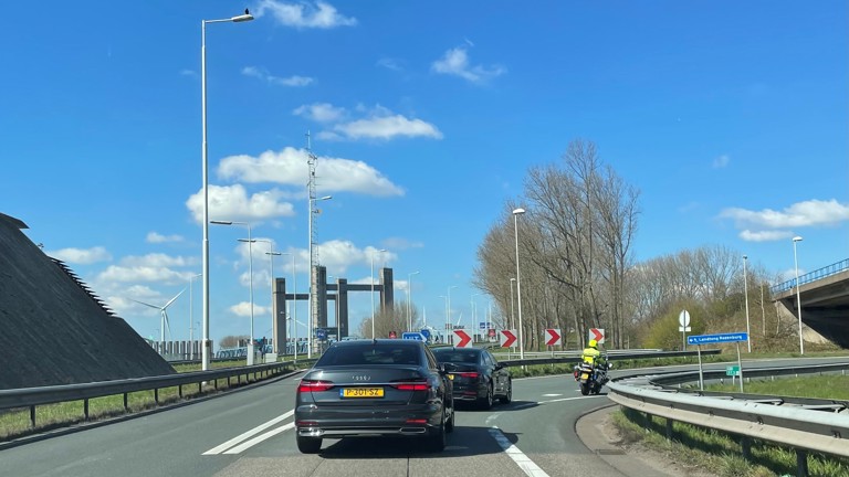 Twee auto's met daarvoor een politiemotor op de afrit van een snelweg