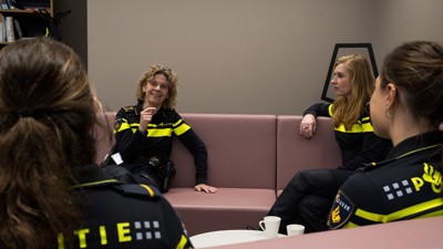 Korpschef Janny Knol zit op een bank in gesprek met drie studenten in uniform