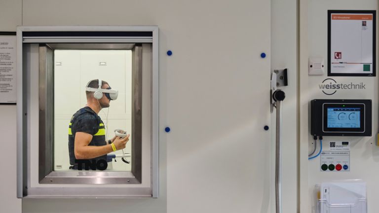 Een blik op student Tom in de klimaatkamer door het glas van de deur heen