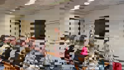 Wim Anker voor een groep studenten, begeleiders en docenten in een klaslokaal