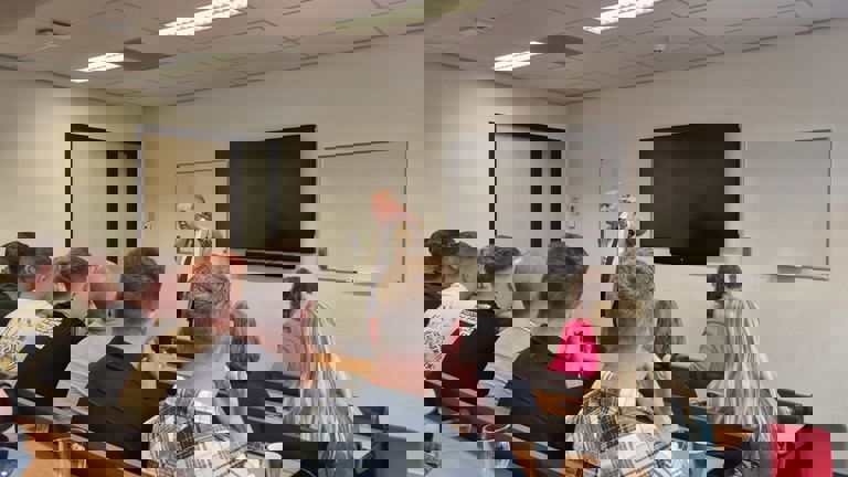 Wim Anker voor een groep studenten, begeleiders en docenten in een klaslokaal