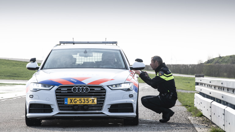 Een politieagent zit op zijn hurken naast een geparkeerde politieauto