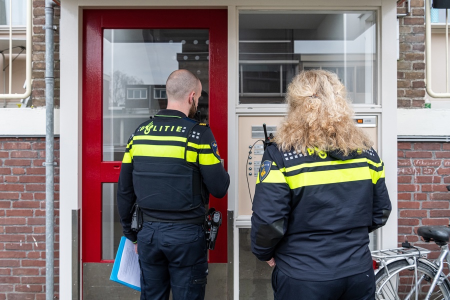 Twee agenten staan voor portaal flatgebouw