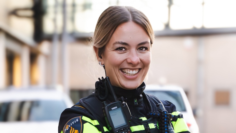 Student Daisy staat lachend met haar armen over elkaar met een politieauto op de achtergrond