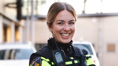 Student Daisy staat lachend met haar armen over elkaar met een politieauto op de achtergrond