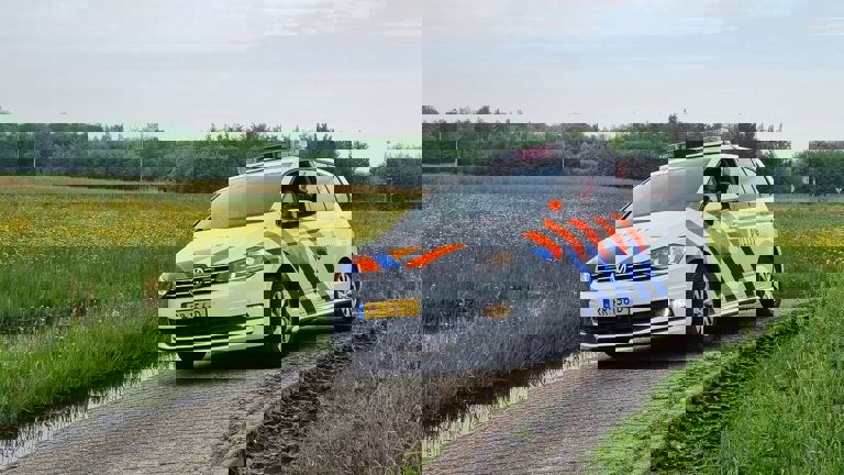 Docent Estée rijdt in een politieauto met het raam open en steekt haar duim omhoog