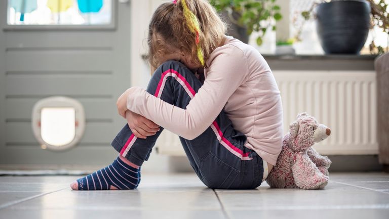 Een jong meisje zit op de grond en is verdrietig