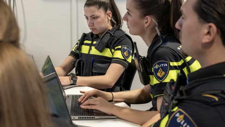 Diverse studenten zitten in uniform aan tafel achter hun laptops