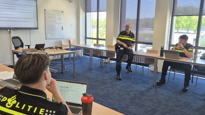 Een aantal studenten in een klaslokaal met de docent op de achtergrond