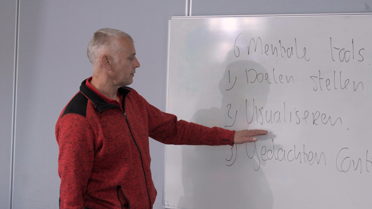 Docent Edwin staat voor een bord waar meerdere mentale tools op staan beschreven