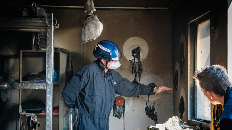 Instructeur onderwijst brandonderzoeker in uitgebrande container