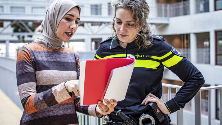 Een politieagent en een vrouw in burgerkleding staan samen in een boek te lezen
