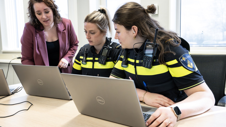 Twee politieagenten zitten achter hun laptop en krijgen uitleg van een manager