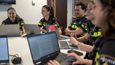 Een groep studenten zit lachend achter hun laptops