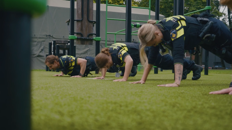 Meerdere politiestudenten in uniform doen push ups op een grasveld