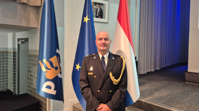 Johan van Lare, vice-president van de Association of European Police Colleges, staat voor drie vlaggen