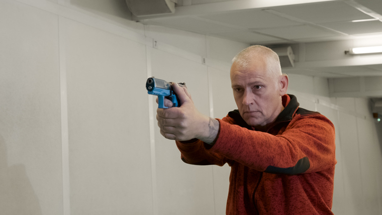 Docent Edwin staat met een nep vuurwapen op de schietbaan