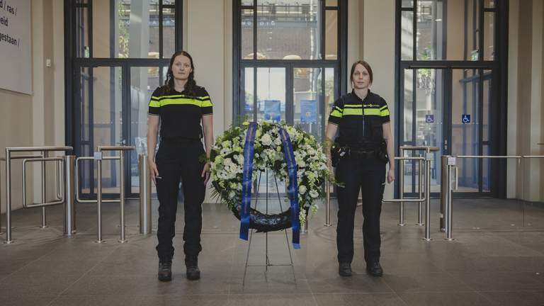 Twee politiestudenten staan naast een krans in de centrale hal van de concernlocatie Apeldoorn