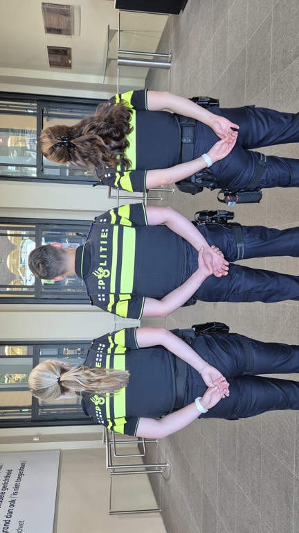 Drie politiestudenten staan in de hal van de Politieacademie Apeldoorn achter een krans