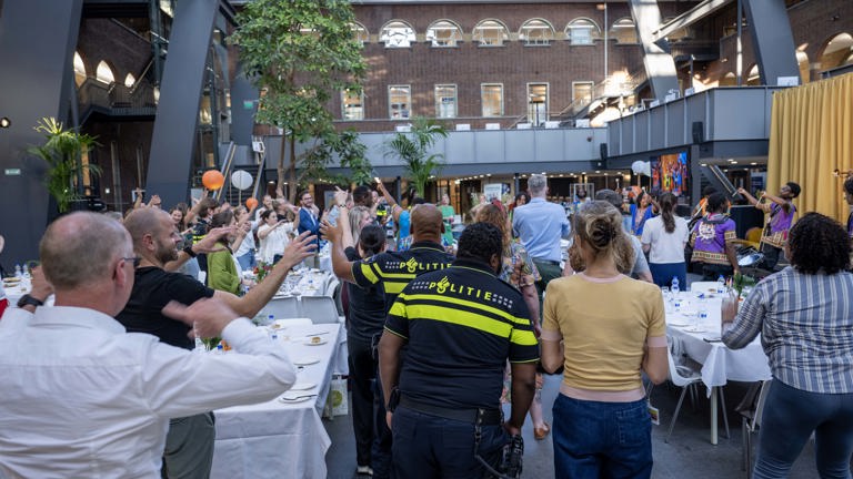 Een grote groep mensen en politieagenten dansen op de muziek van een brassband