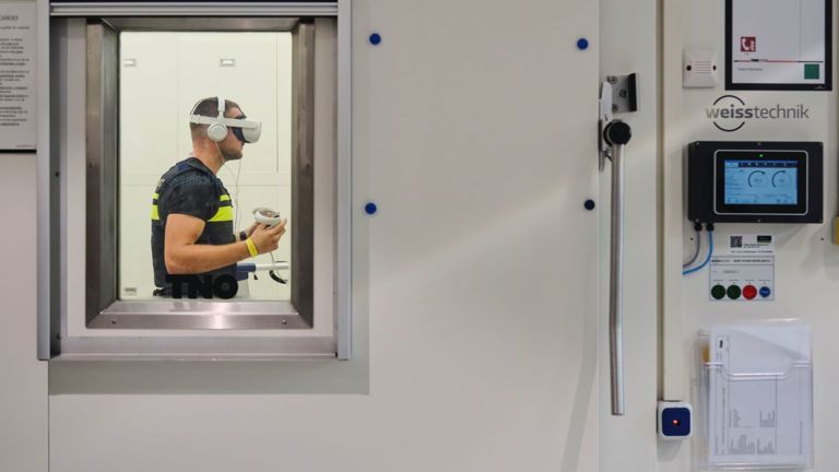 Doorkijkje door het glas van de deur van de klimaatkamer waar student Tom staat