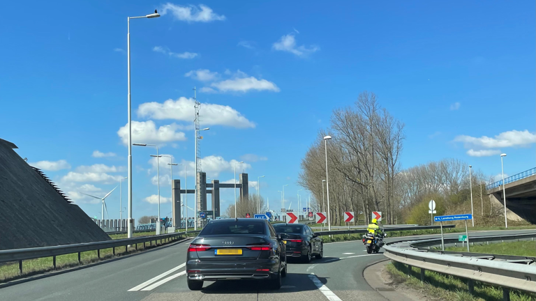 Twee auto's met daarvoor een politiemotor op de afrit van een snelweg