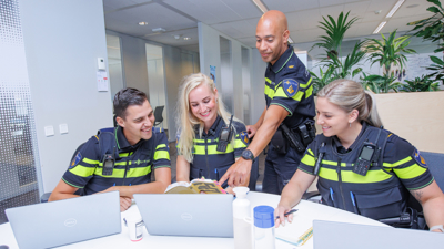 Een docent en drie politiestudenten kijken samen op een laptop en lachen