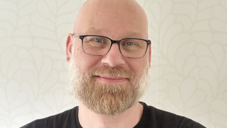 Docent Tim lacht naar de camera met zijn armen over elkaar