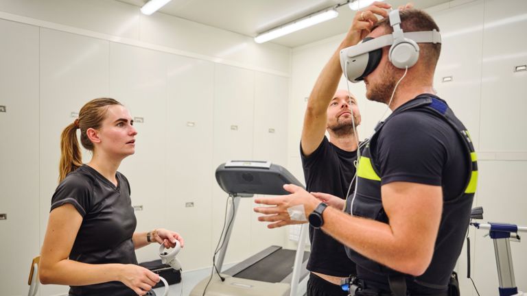 Twee onderzoekers staan naast student Tom in de klimaatkamer waar hij een VR-bril op krijgt